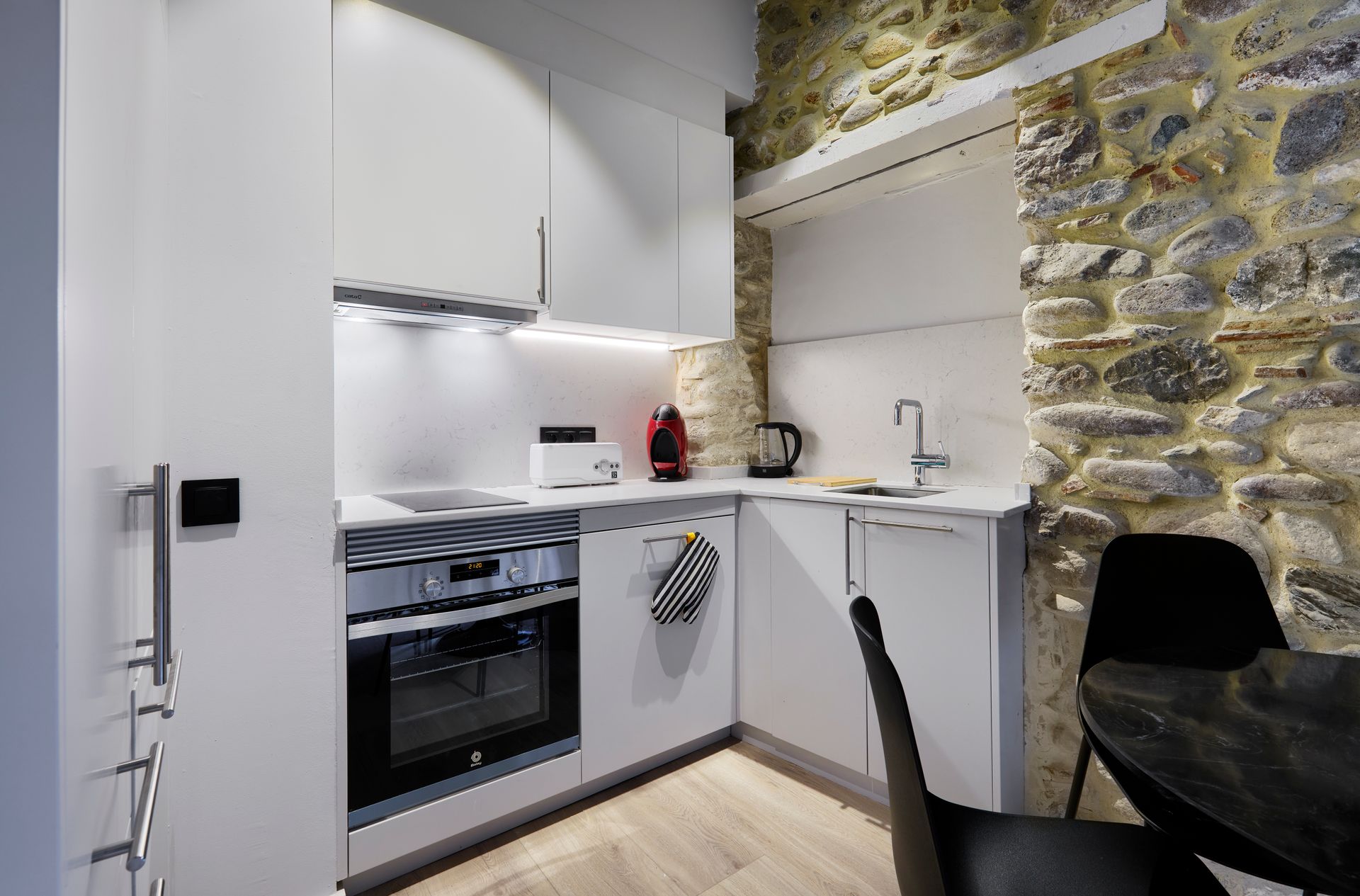 A kitchen with white cabinets and a stone wall.