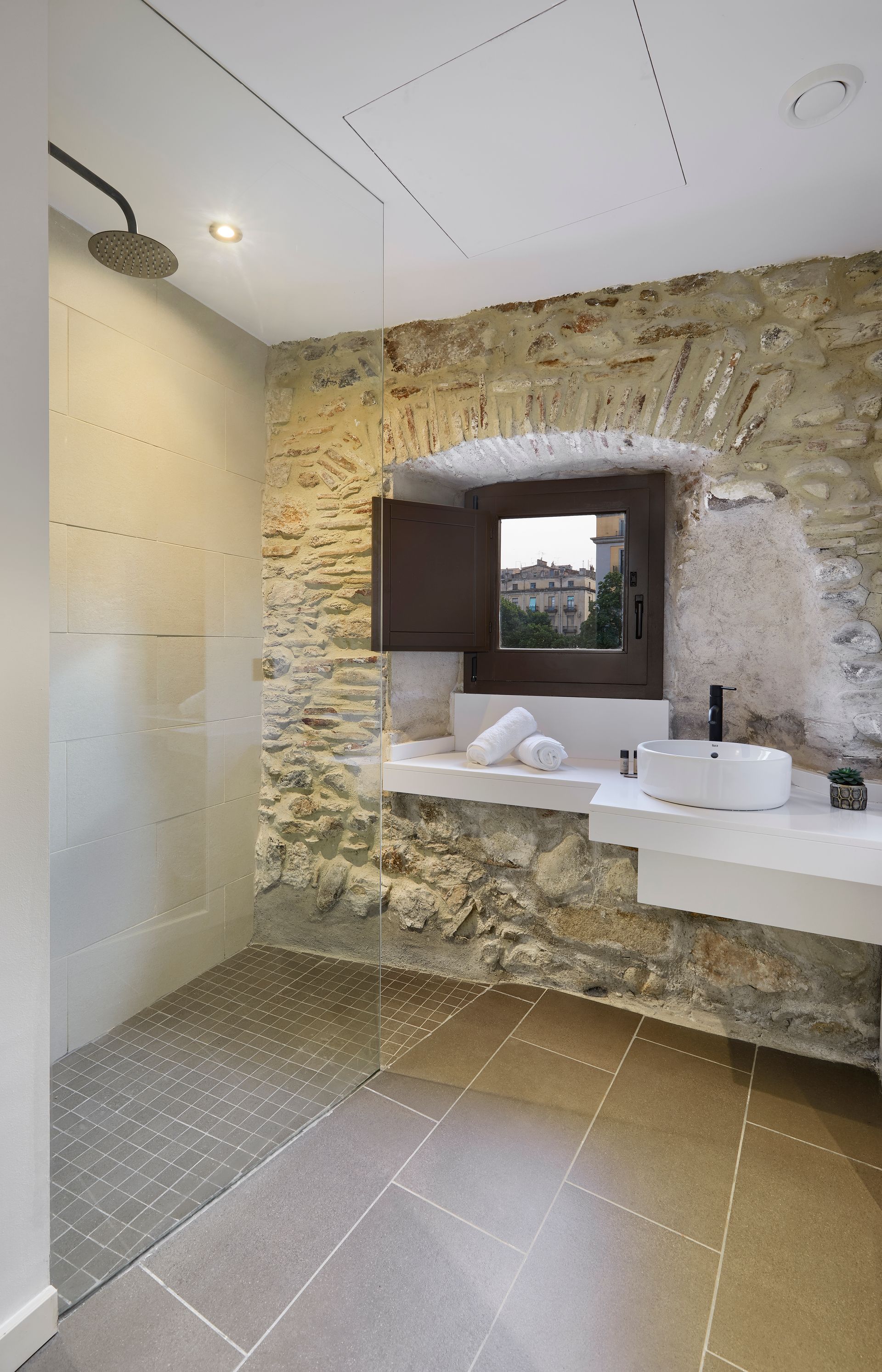 A bathroom with a stone wall , a sink , and a walk in shower.