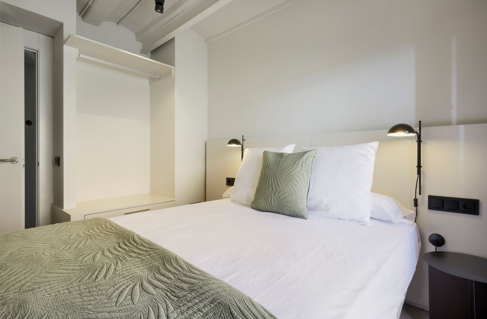 A bed with white sheets and green pillows in a hotel room.