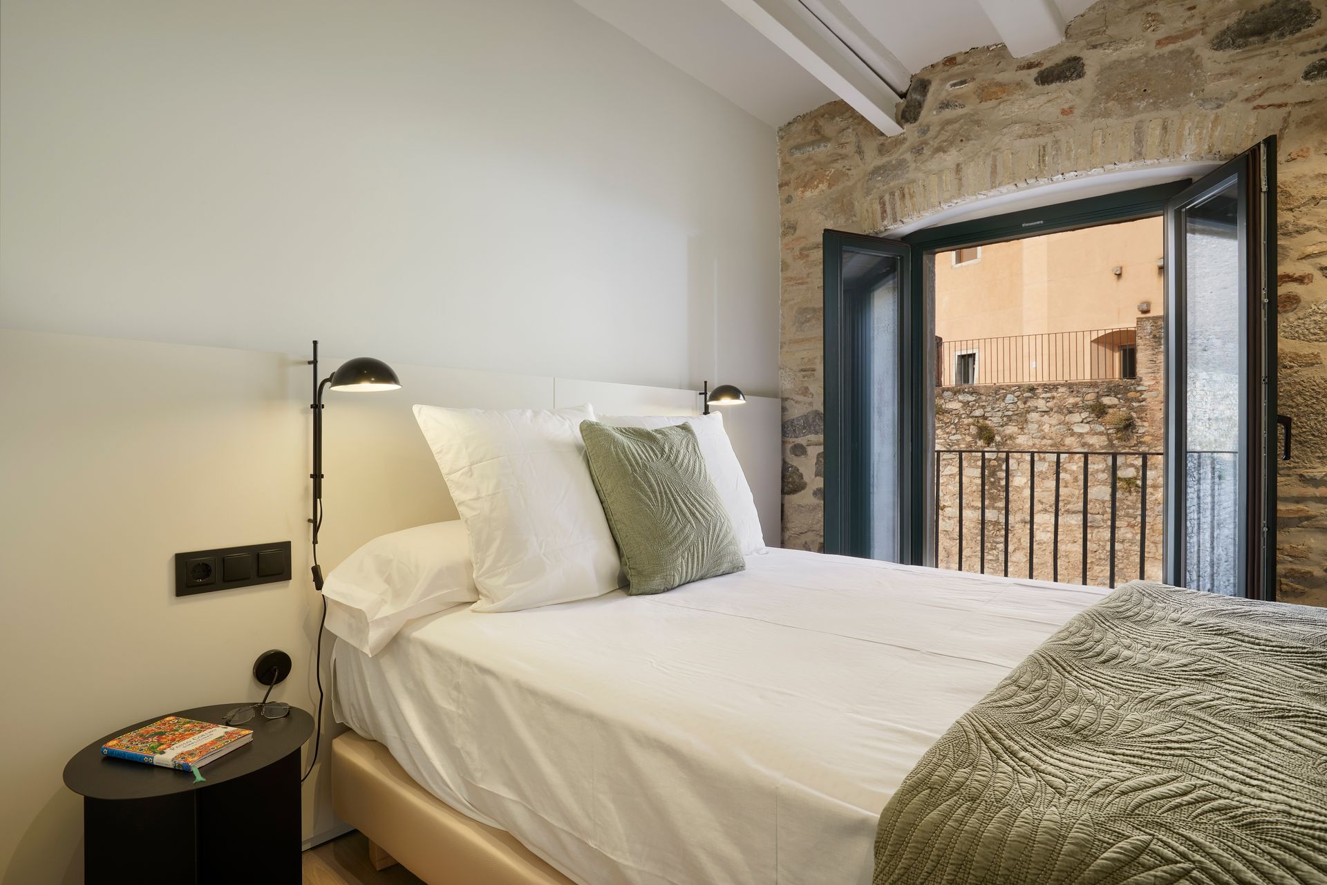 A bedroom with a bed , nightstand , lamp and a large window.