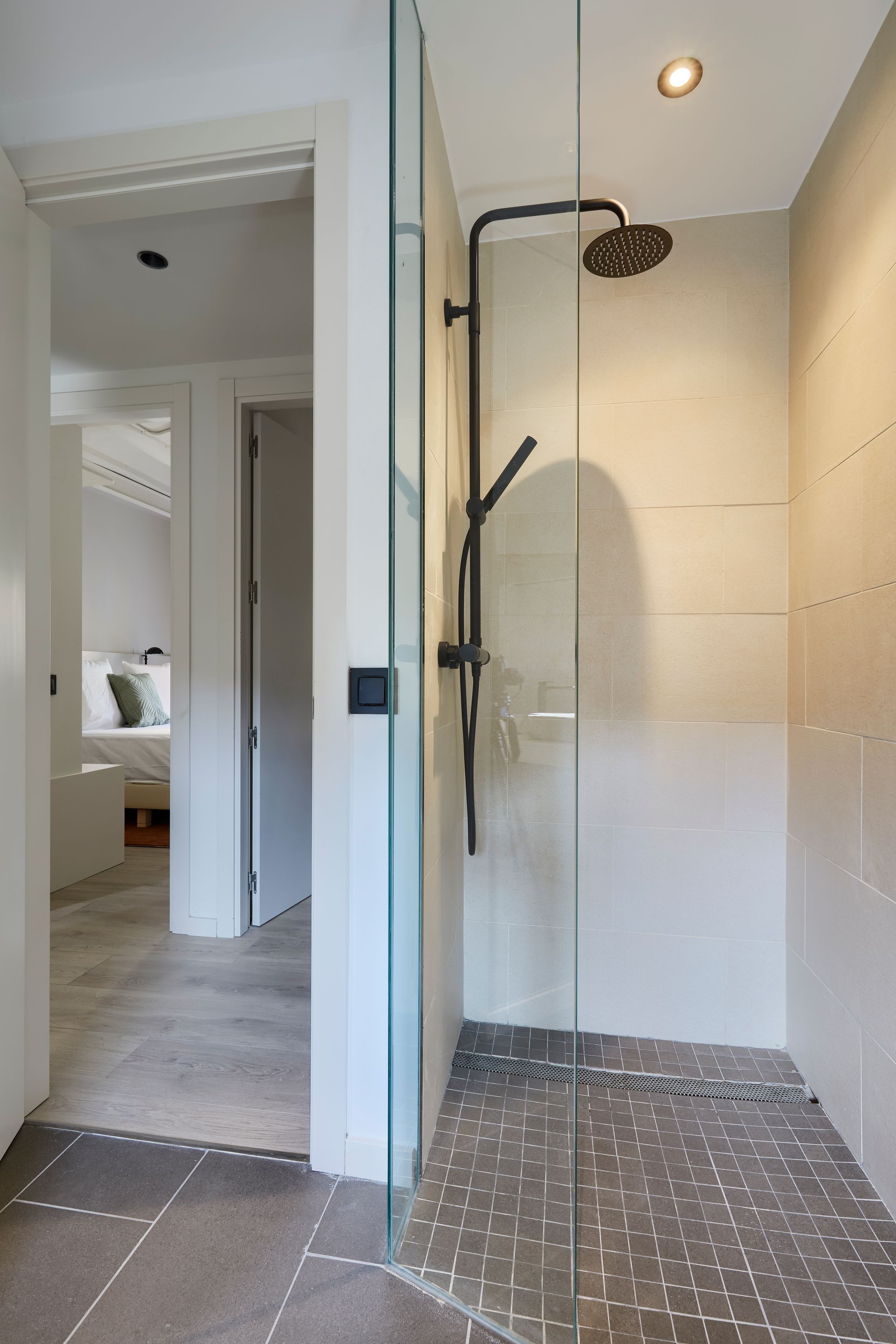 A walk in shower with a glass door and a black shower head.