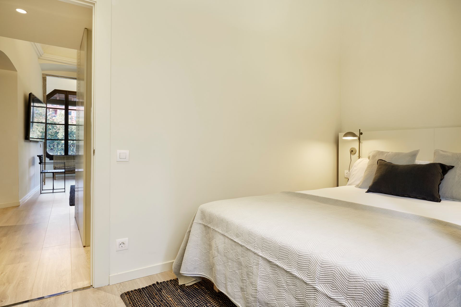 A bedroom with a bed and a door leading to a living room.