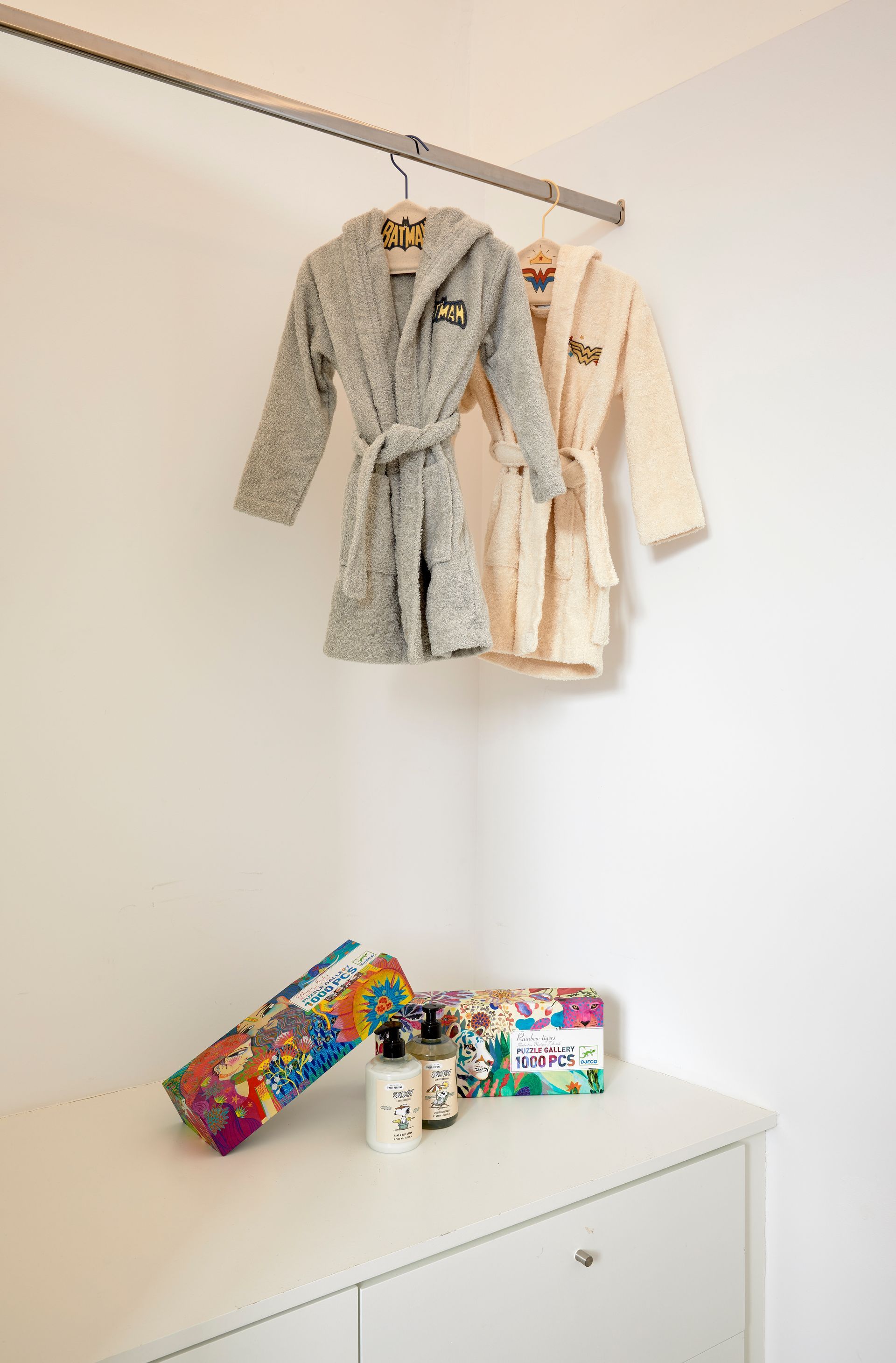Two bathrobes are hanging on a rack in a bathroom next to a dresser.
