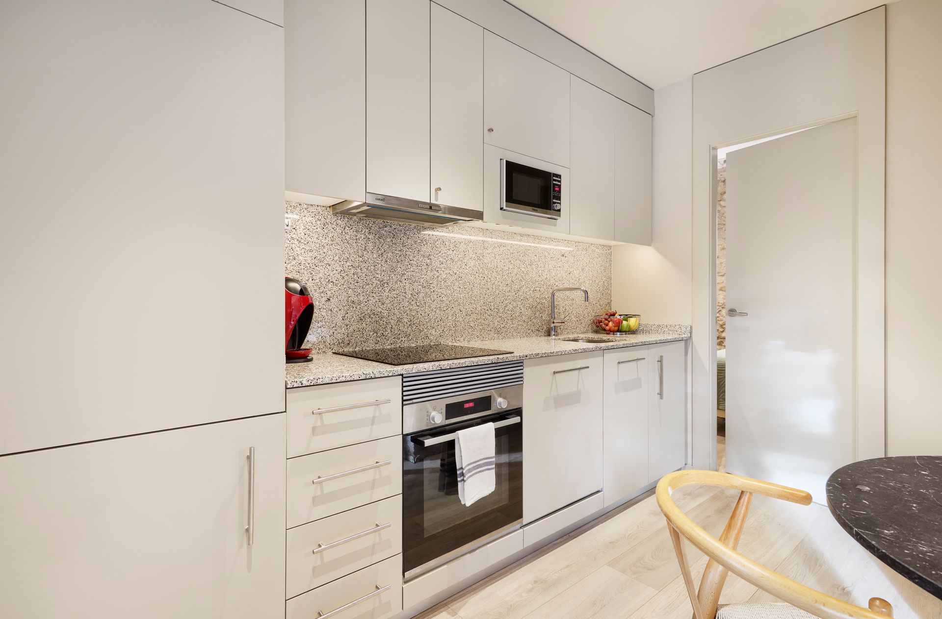 A kitchen with white cabinets , a stove , a microwave and a table.