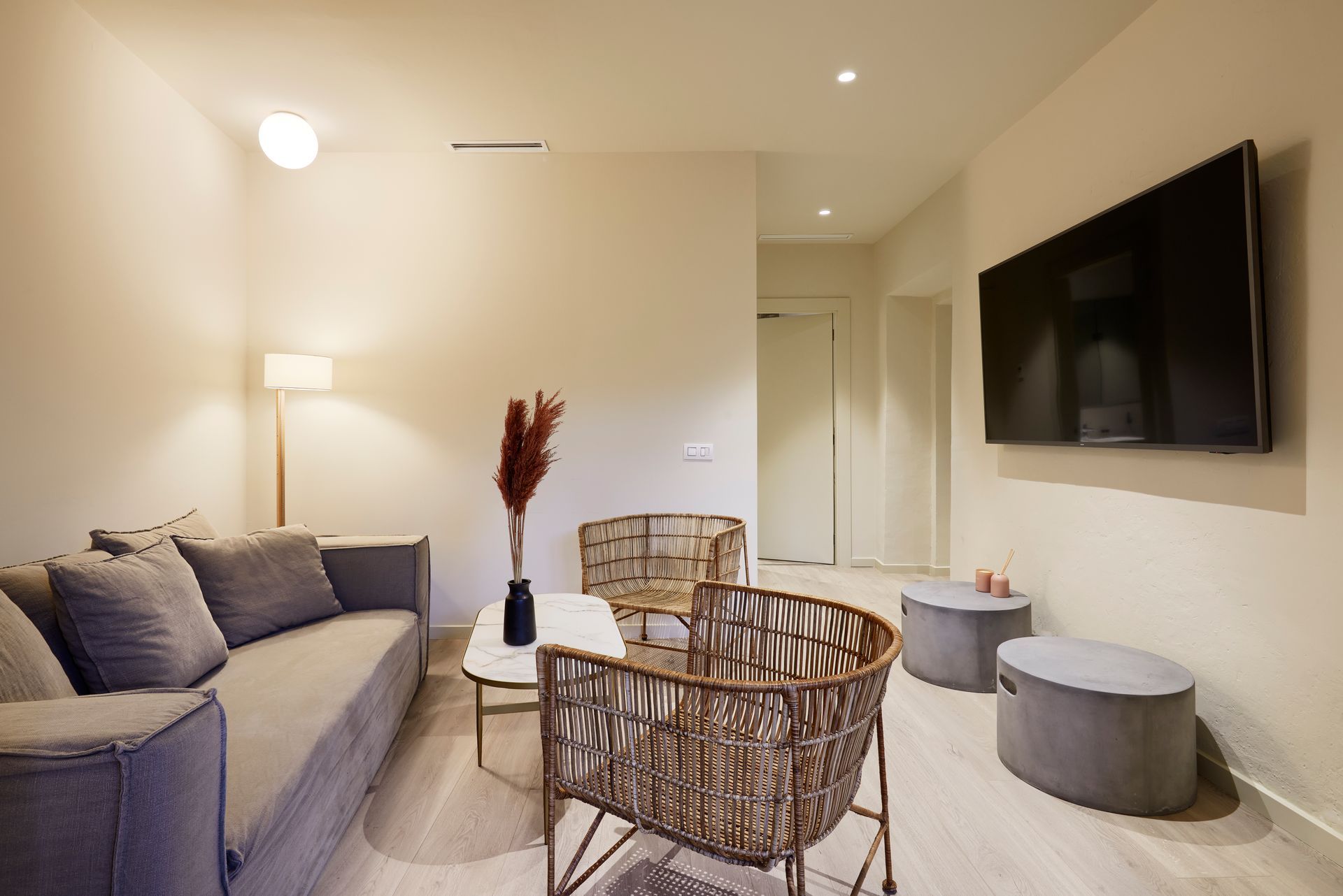A living room with a couch , chairs , ottomans and a flat screen tv.