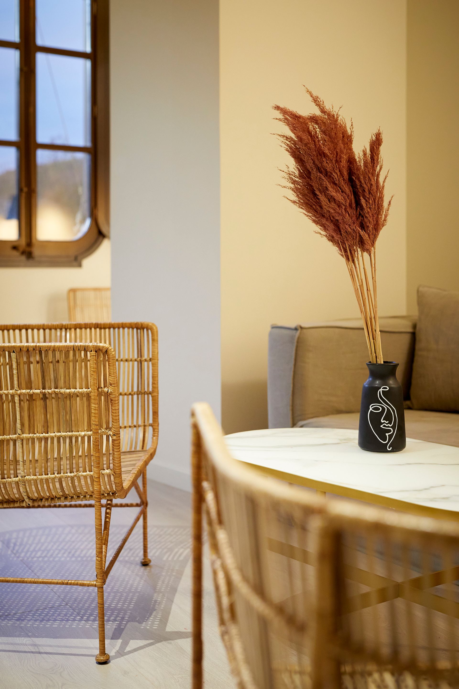 A vase of dried flowers is sitting on a table in a living room next to a couch.