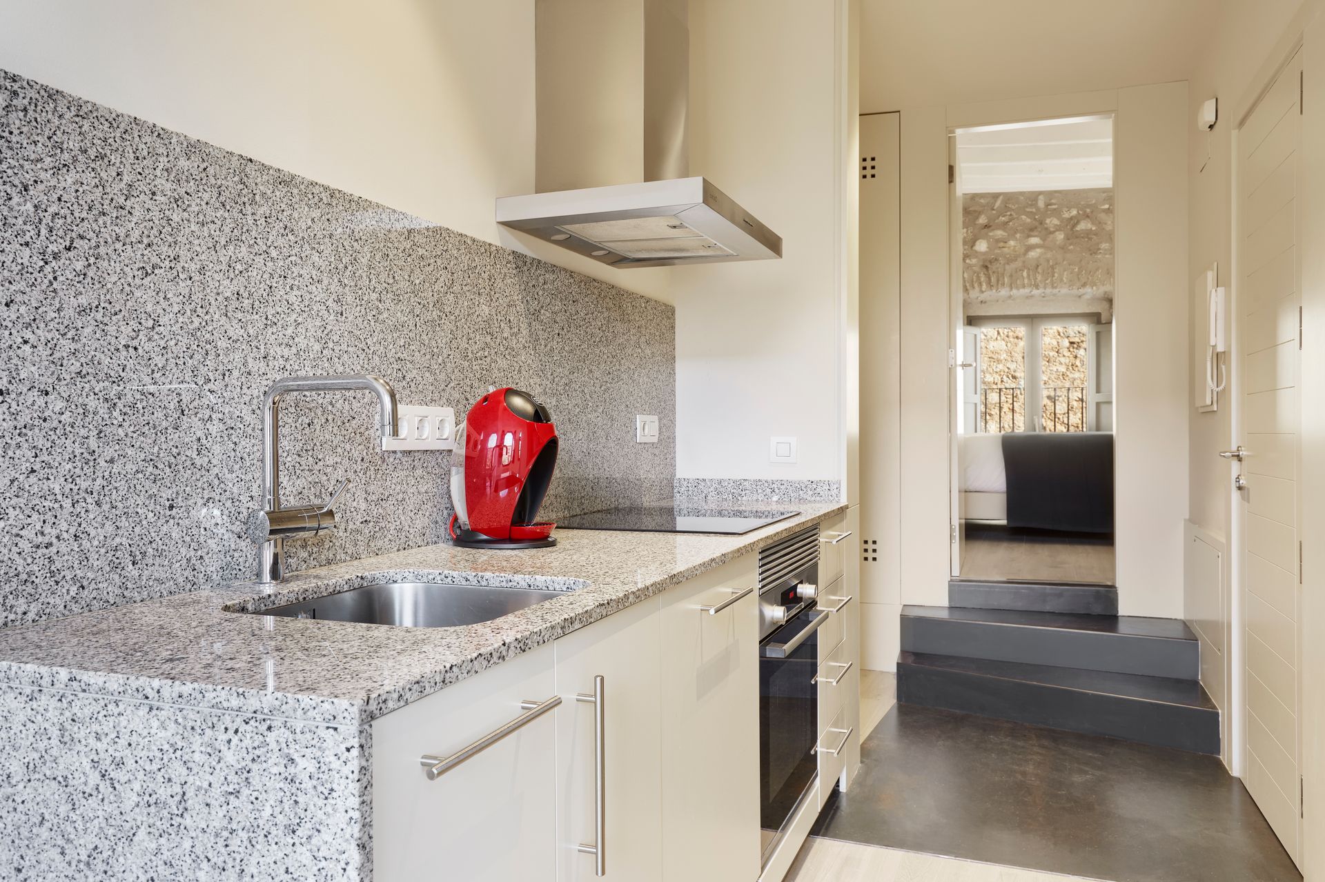 A kitchen with granite counter tops , stainless steel appliances and a red coffee maker.