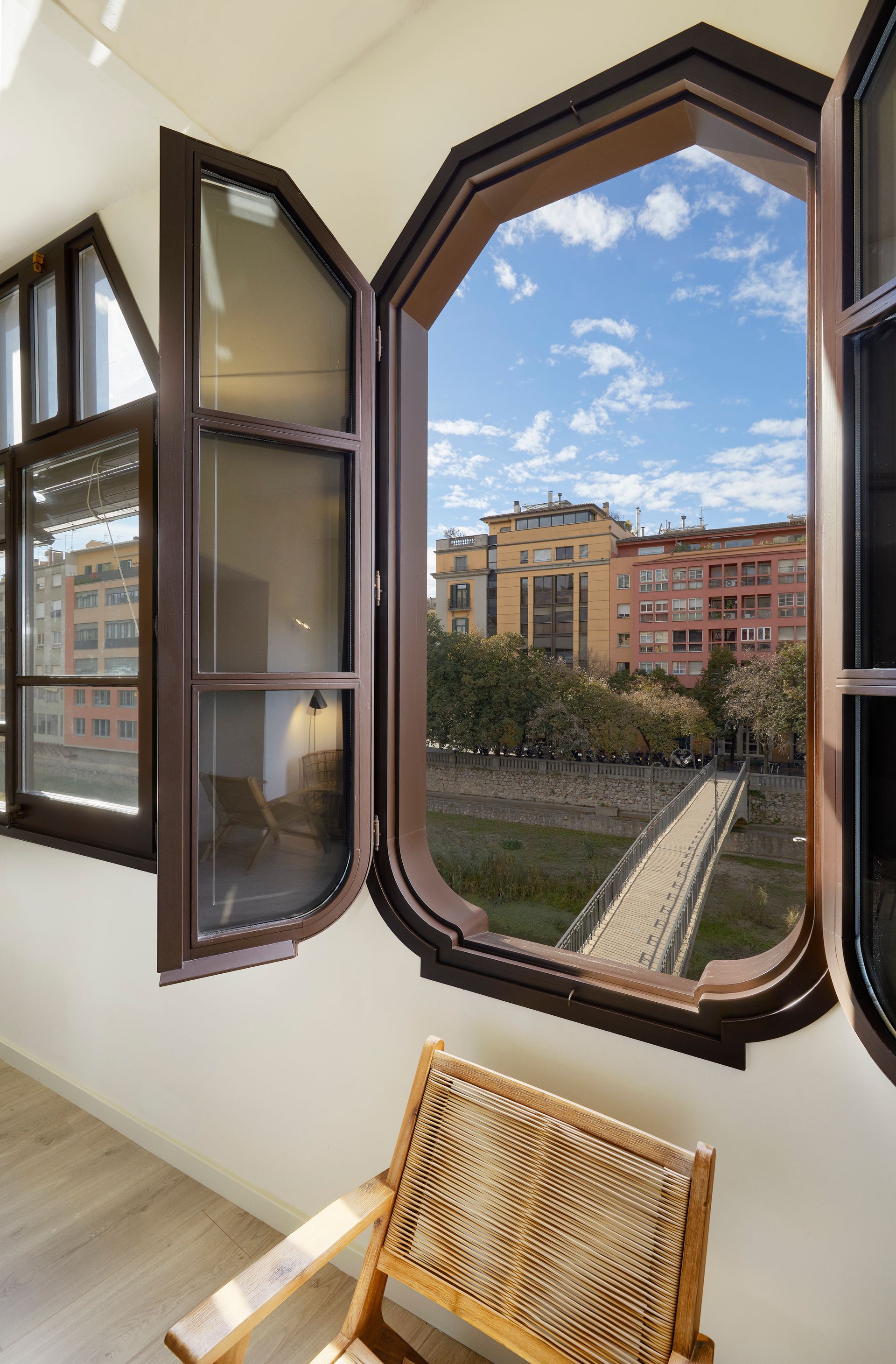 A chair is sitting in front of an open window with a view of a city.