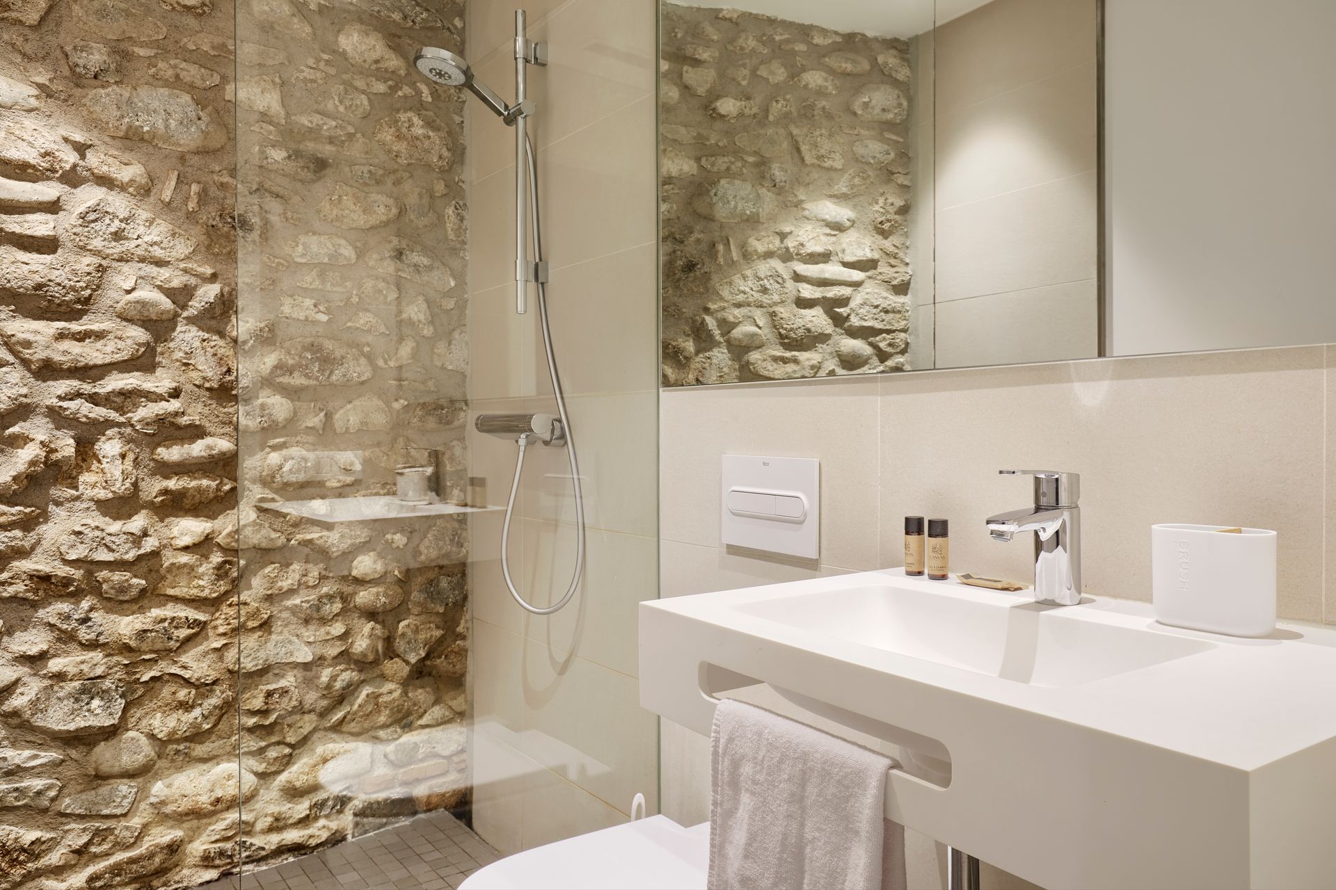 A bathroom with a stone wall , a sink , toilet and shower.