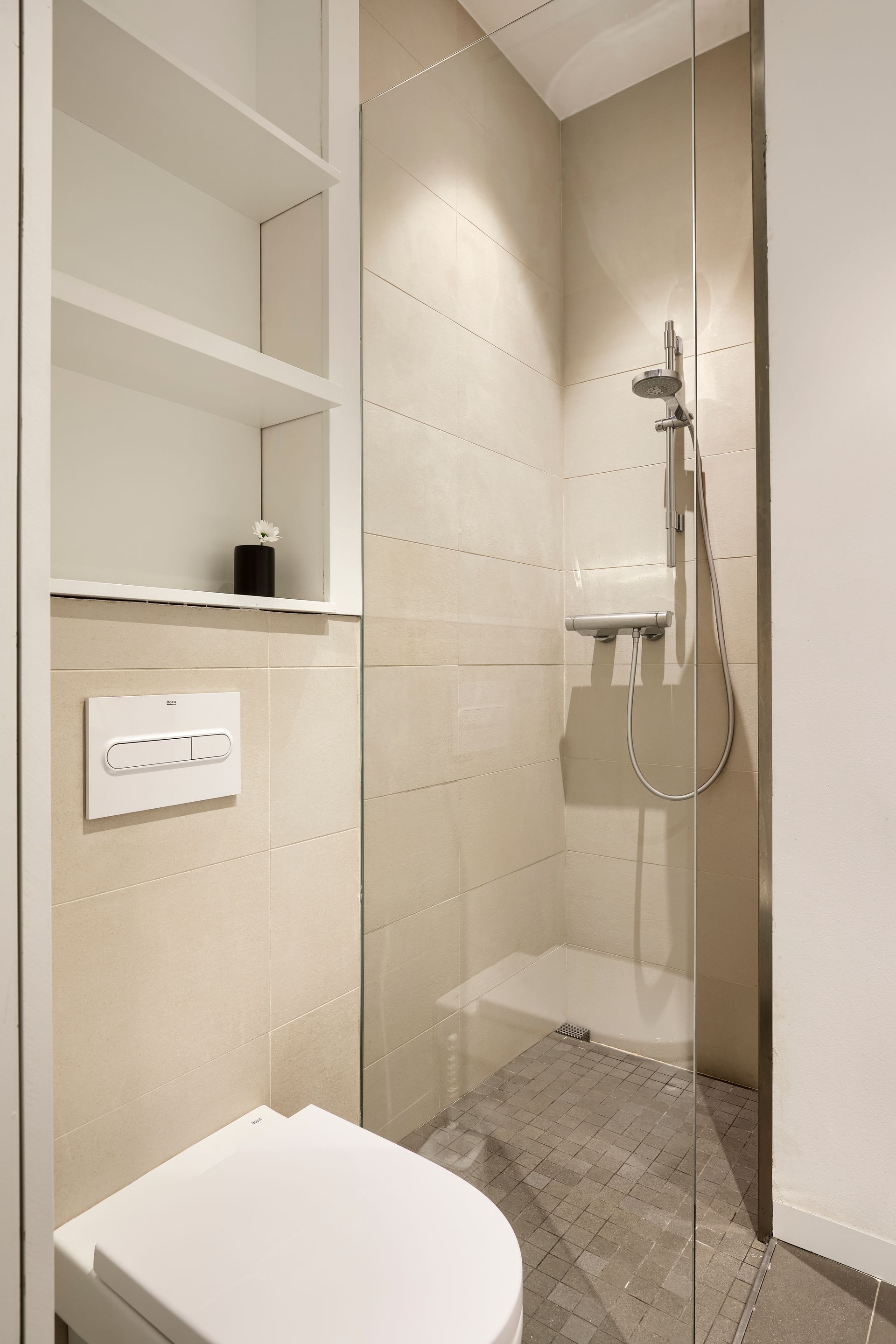 A bathroom with a toilet , shower and shelves.