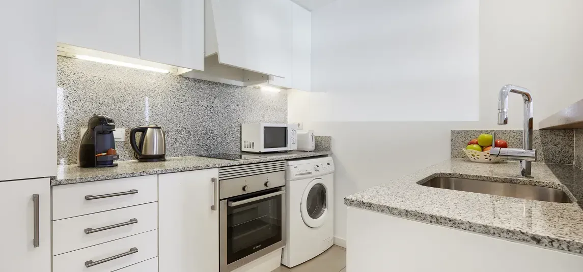 A kitchen with a sink , oven , microwave and washing machine.
