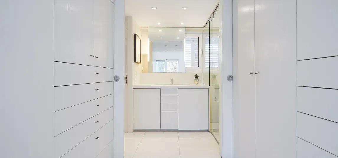 A hallway leading to a bathroom with white cabinets and a sink.