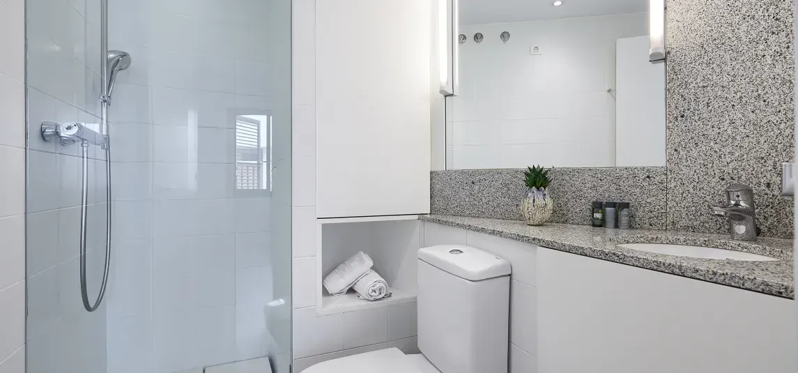 A bathroom with a toilet , sink , shower and mirror.