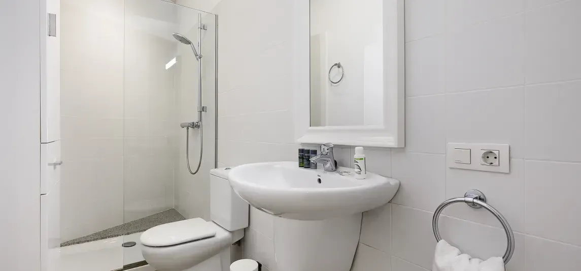 A bathroom with a toilet , sink , mirror and shower.