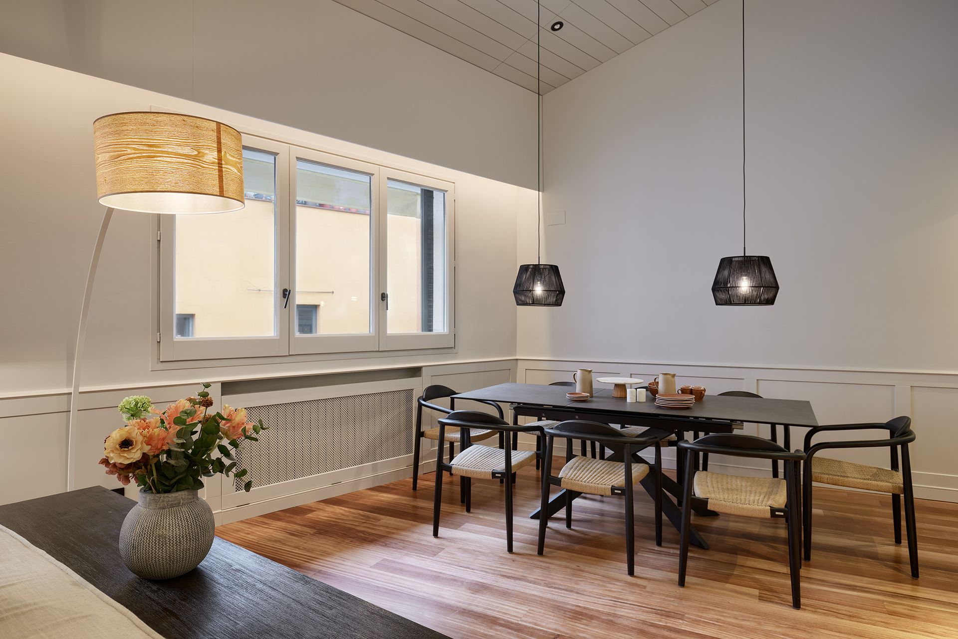 A dining room with a table and chairs and a vase of flowers on the table.