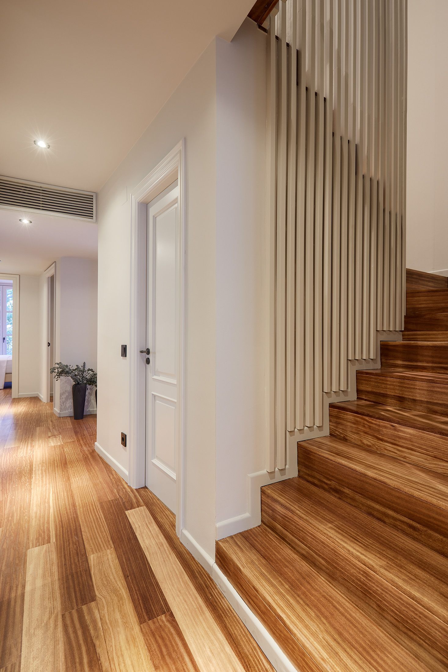A hallway with wooden floors and stairs in a house.