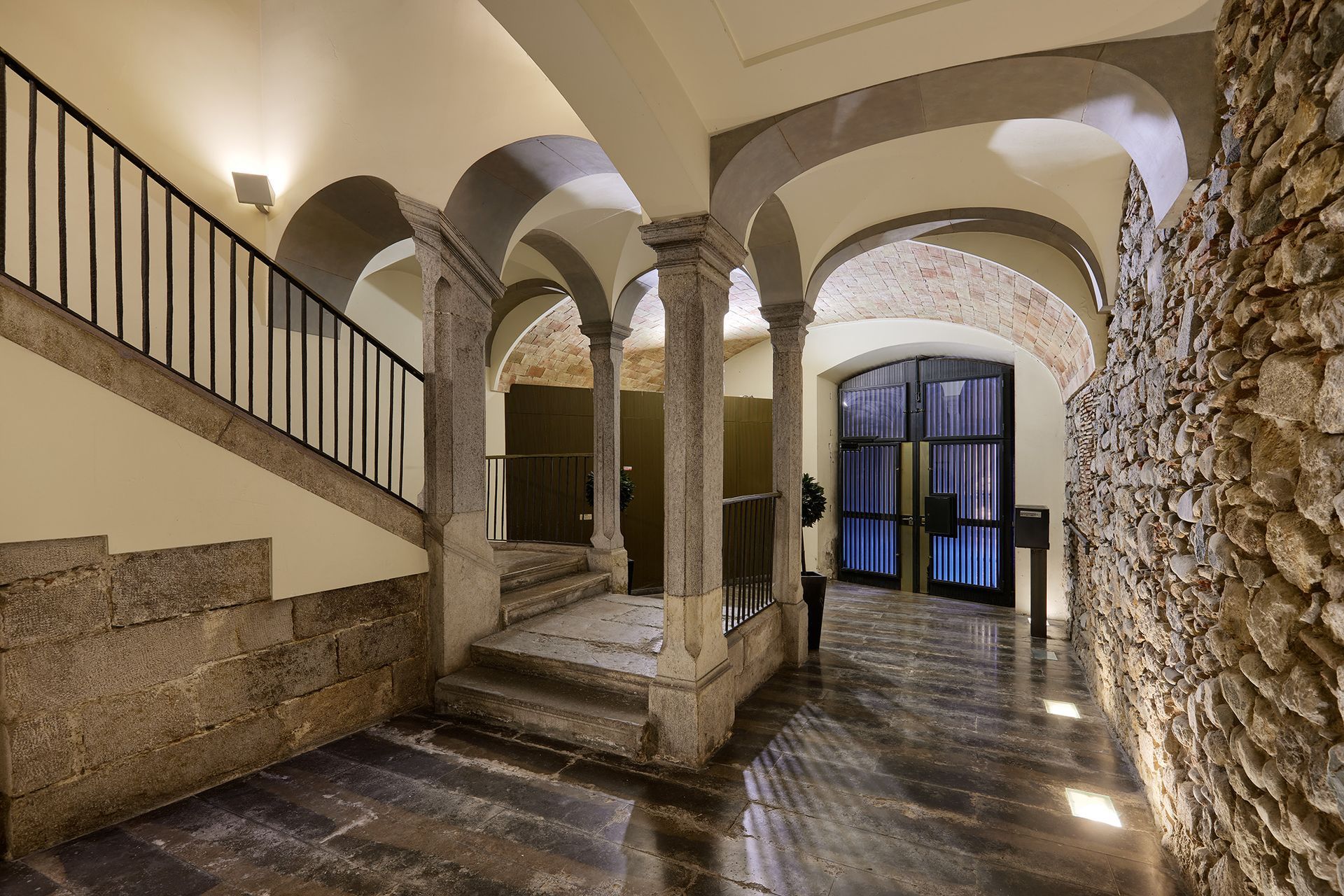 A hallway with arches and stairs and a stone wall