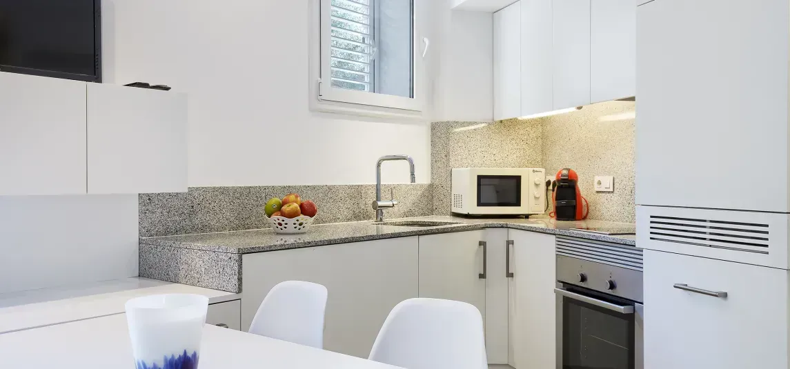 A kitchen with white cabinets , a stove , a microwave , a sink and a table.