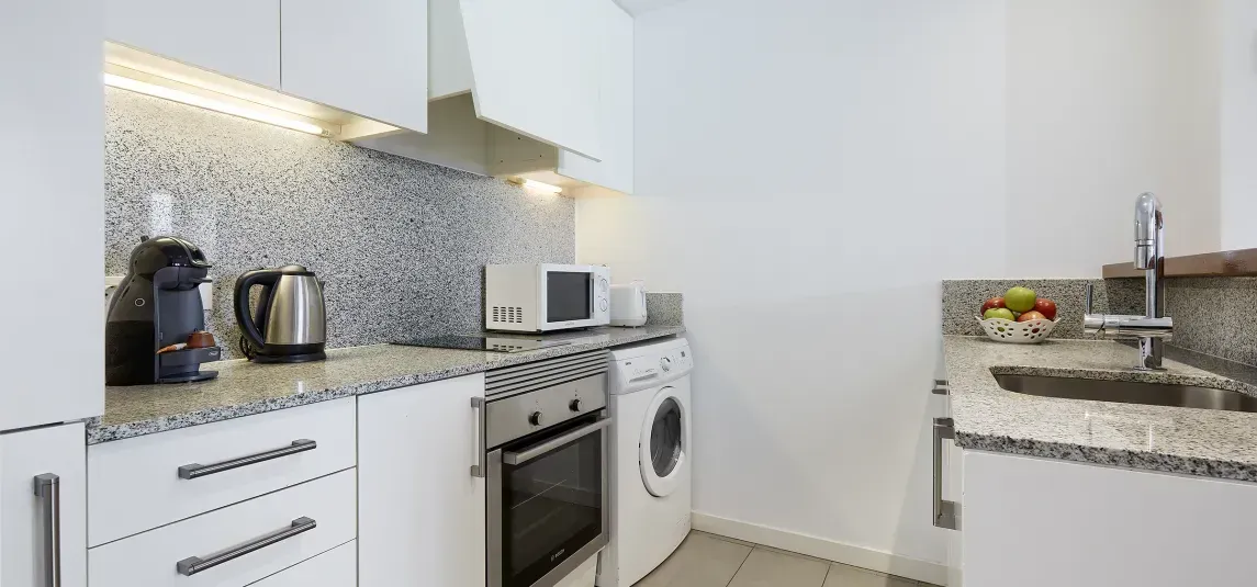A kitchen with white cabinets , a washing machine , a microwave , and a sink.