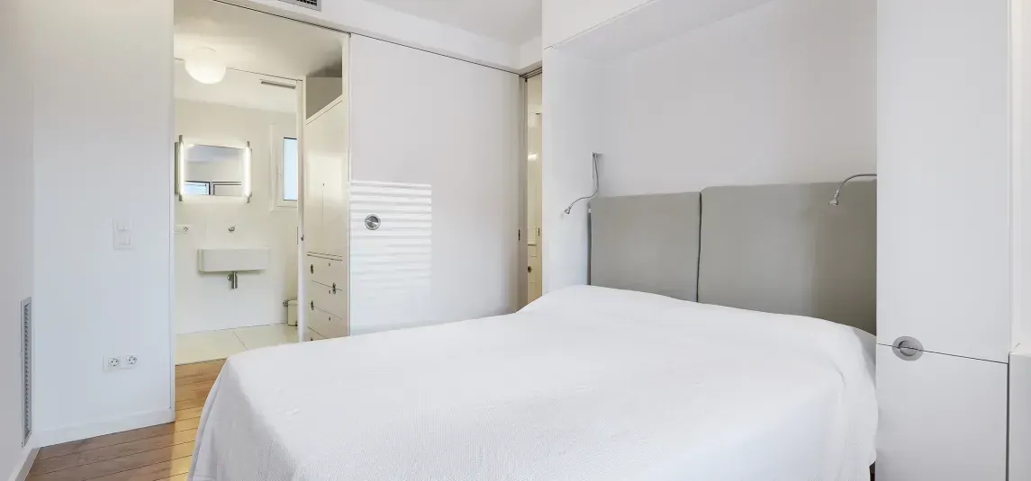 A bedroom with a bed and a bathroom in the background.