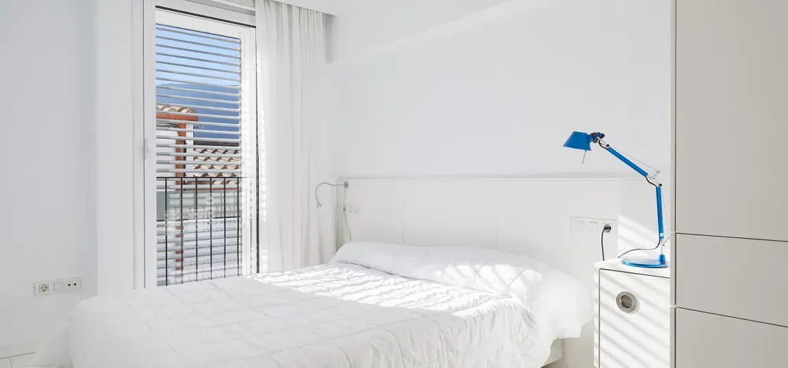 A bedroom with a bed , nightstand , lamp and window.