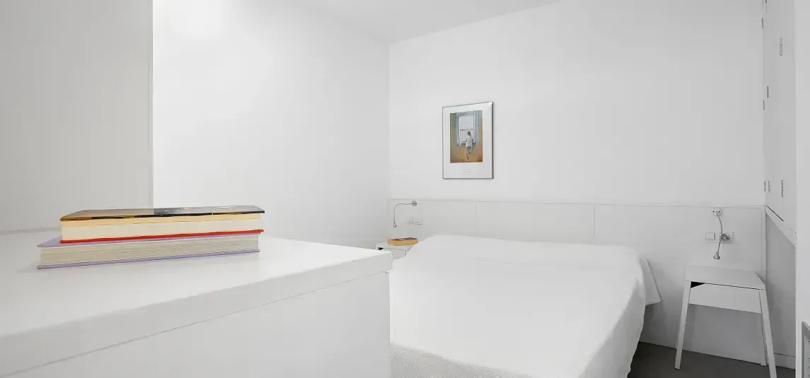 A bedroom with a bed and a stack of books on a table.