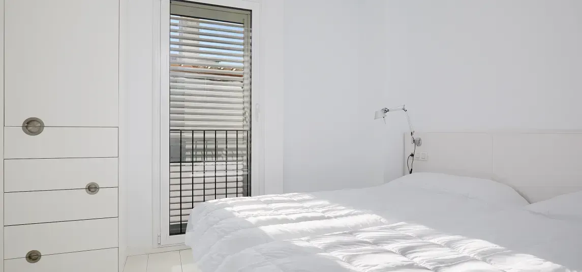 A bedroom with a bed and a window with blinds.