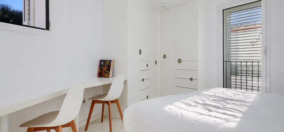 A bedroom with a bed , desk , chairs and a balcony.