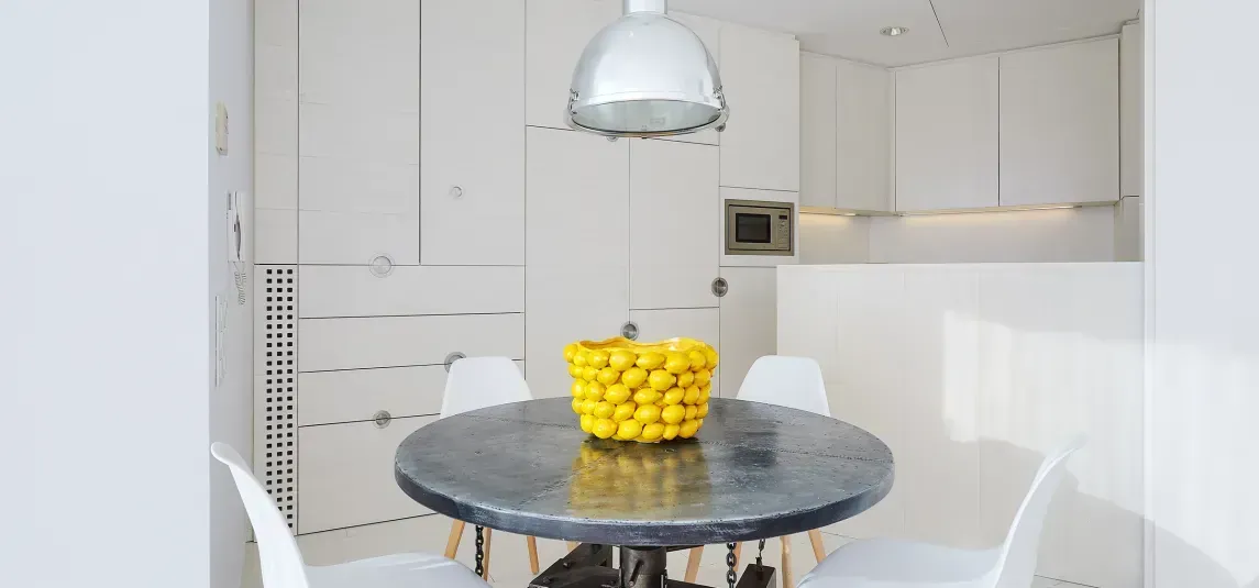 A kitchen with a round table and chairs and a bowl of lemons on it.