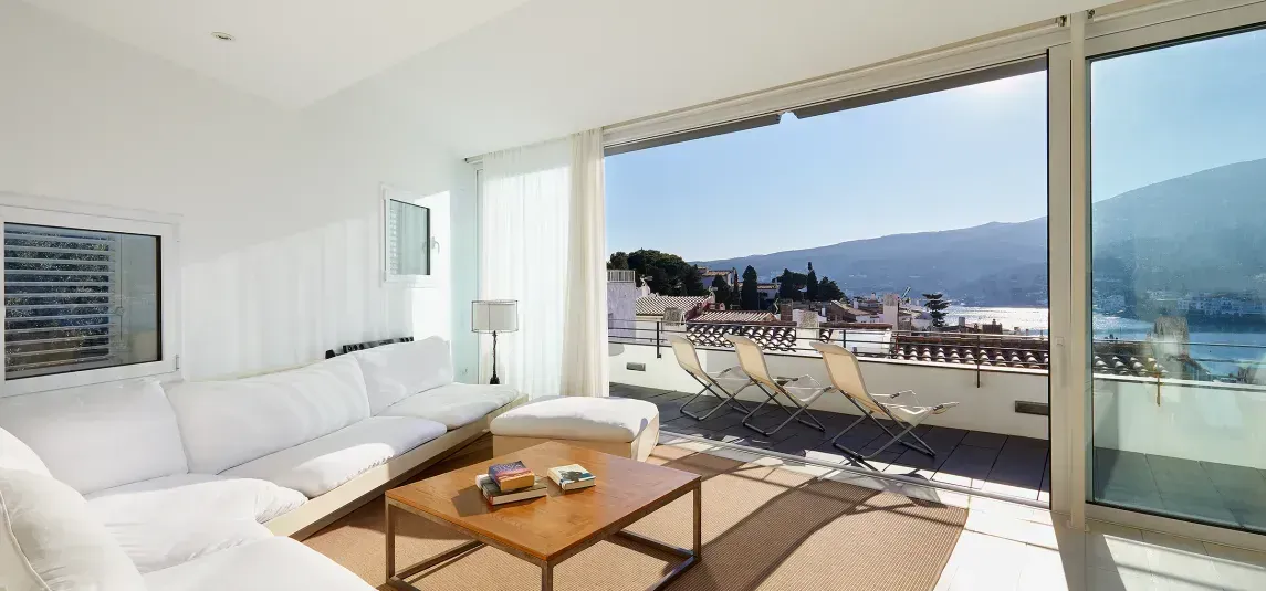 A living room with a couch , table , chairs and a view of the ocean.