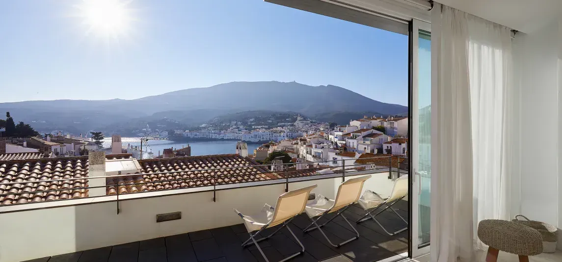 A view of a city from a balcony with chairs and a mountain in the background.