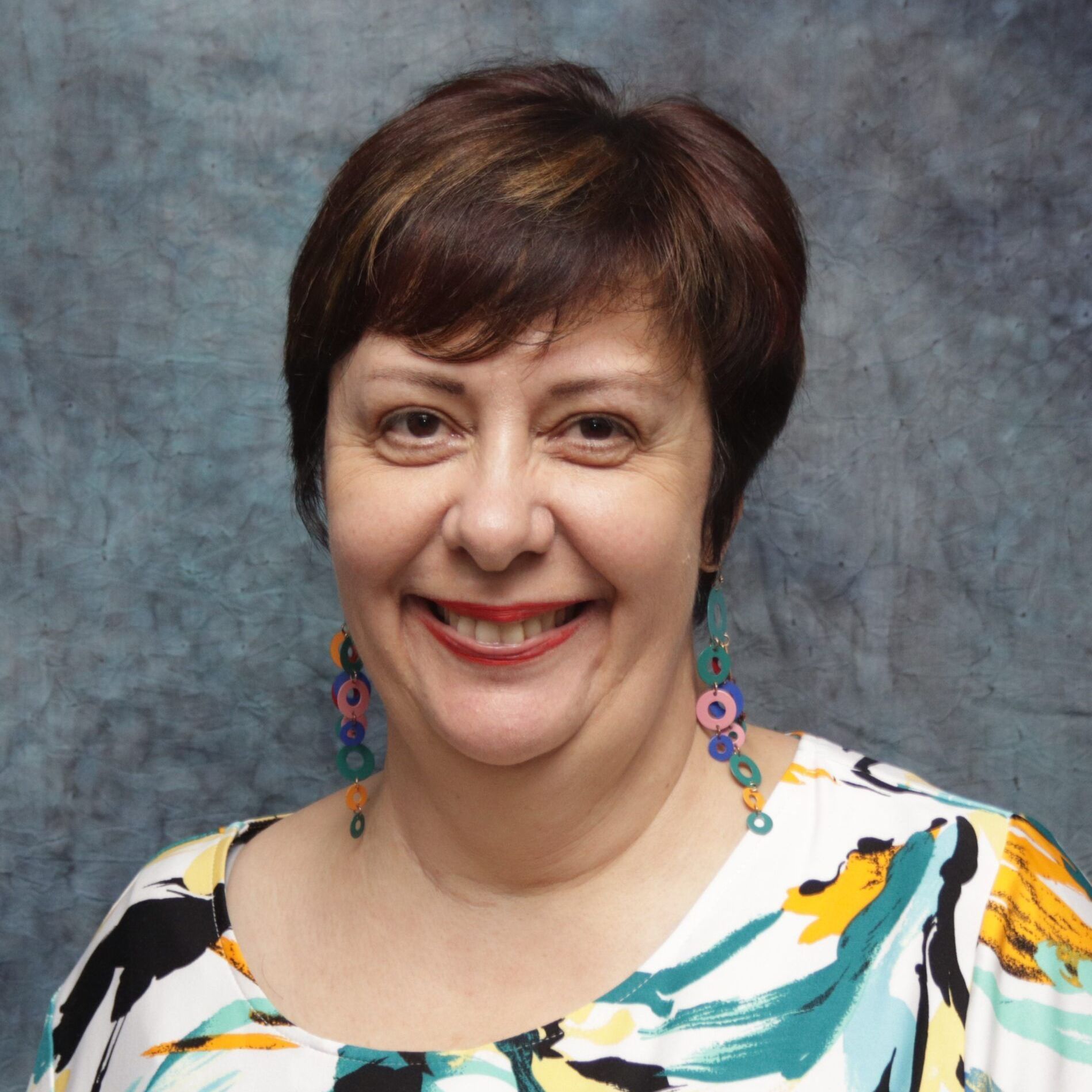 A woman wearing a colorful shirt and earrings smiles for the camera