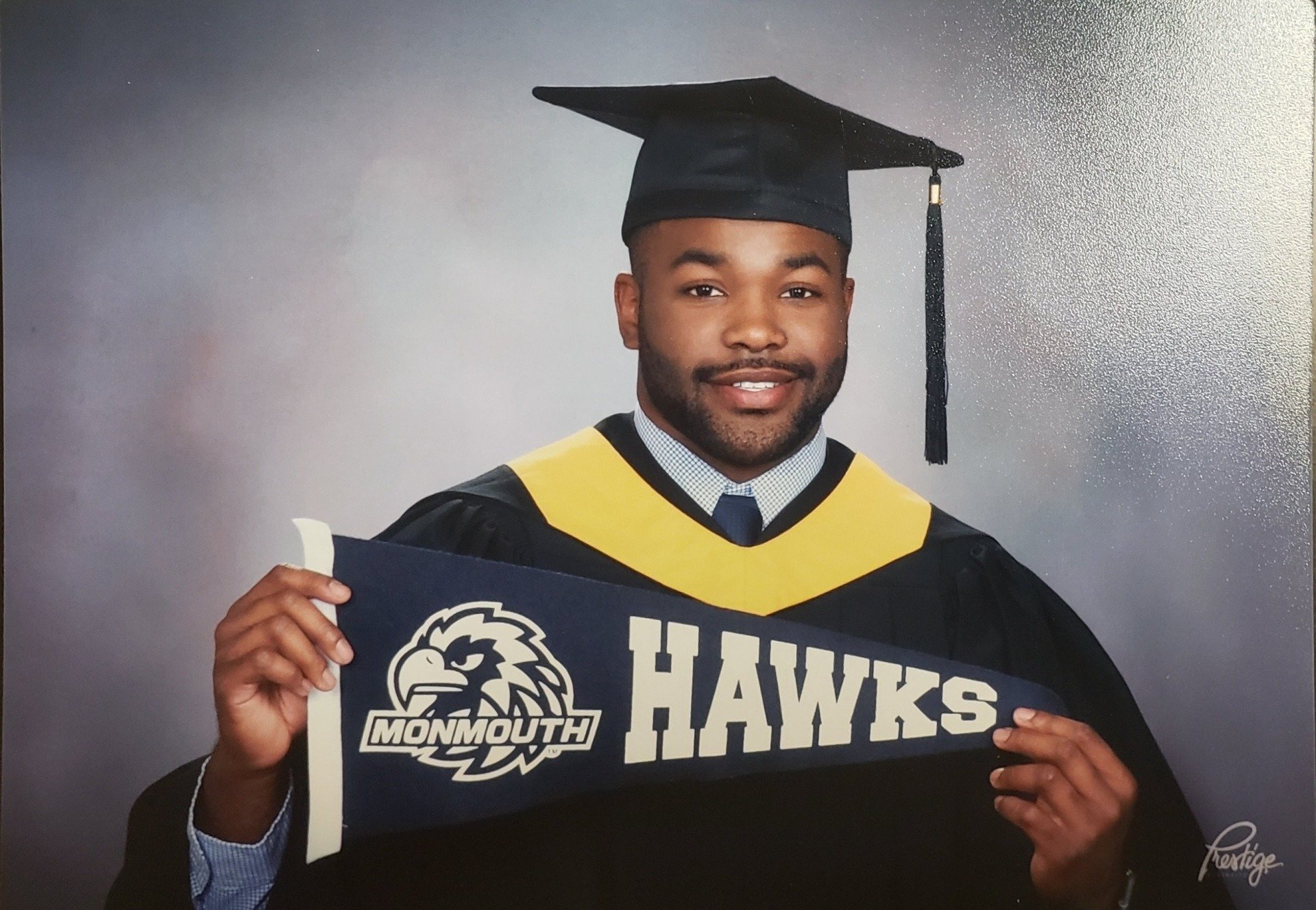 A man in a cap and gown is holding a banner that says monmouth hawks
