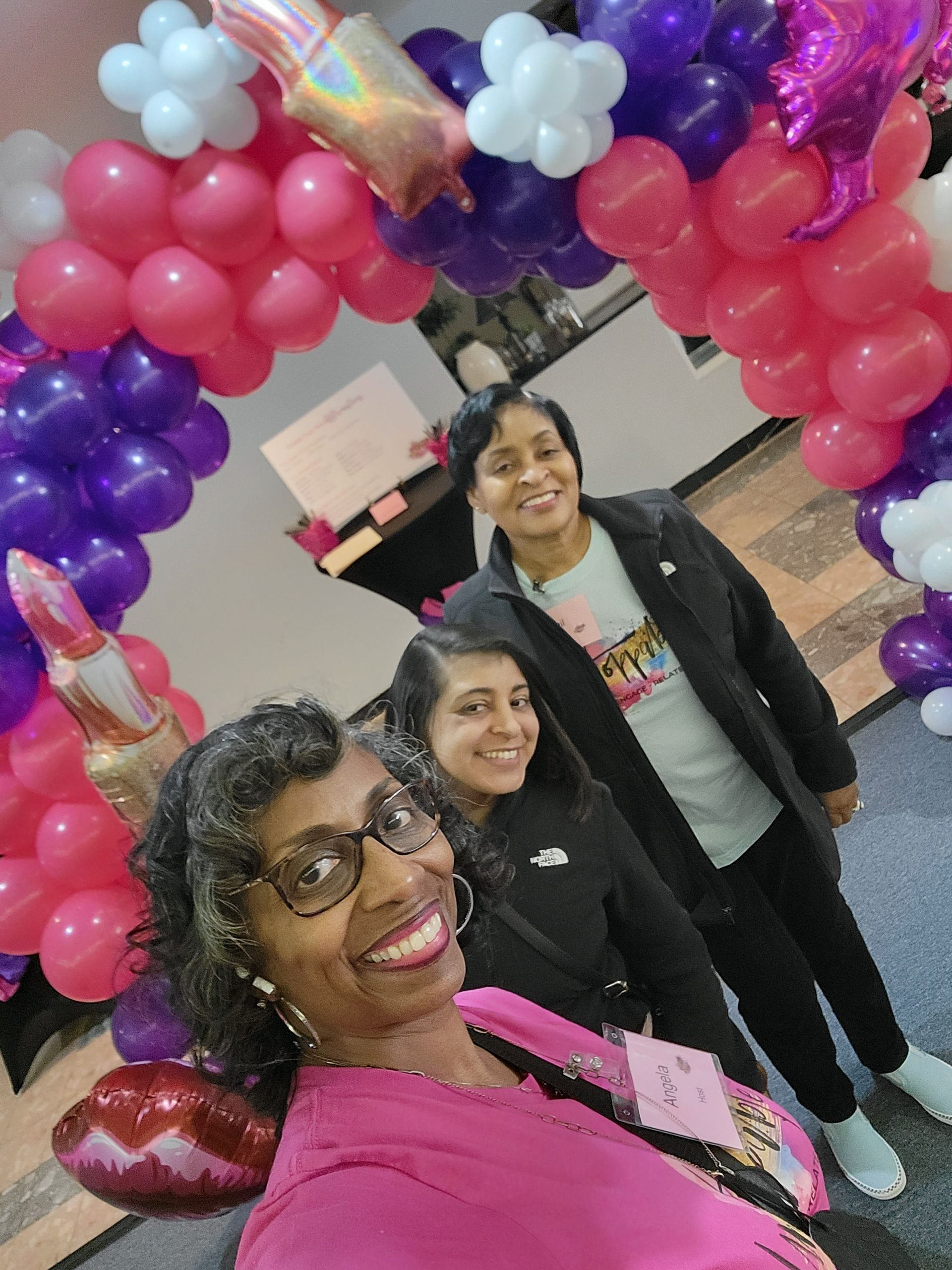 Three women are posing for a picture in front of a balloon arch.