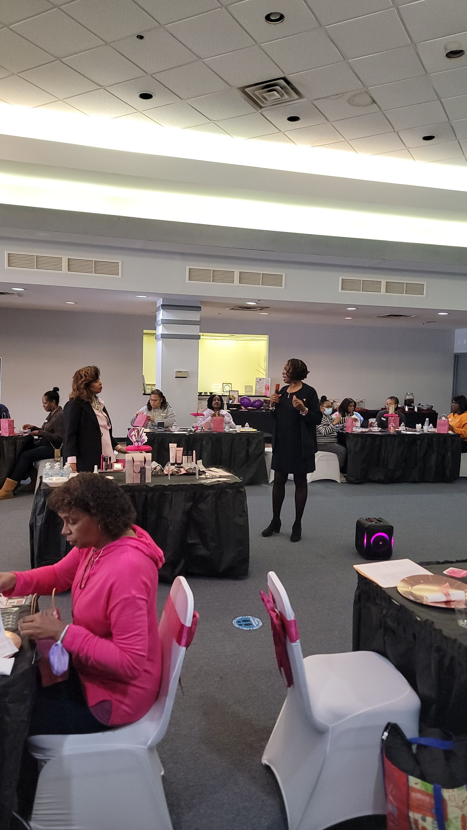 A woman in a pink jacket is sitting at a table in a large room.