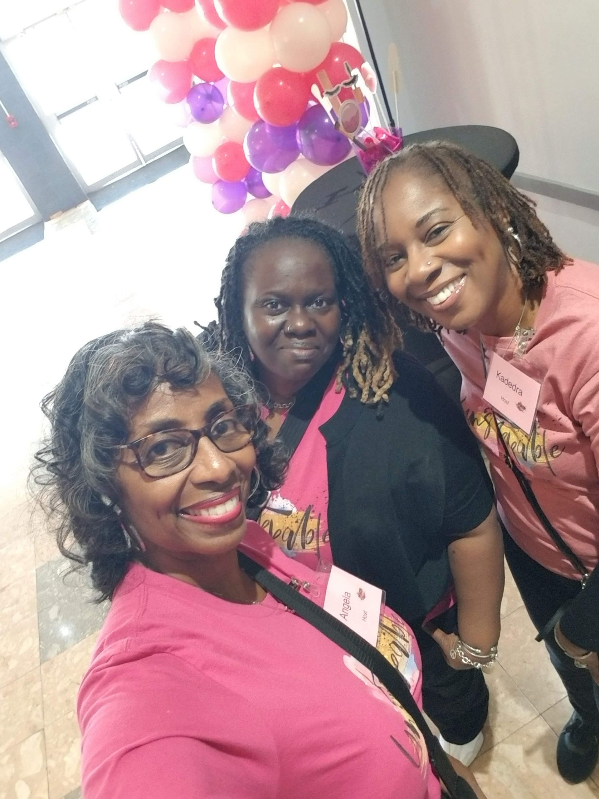 Three women are posing for a picture in front of balloons.