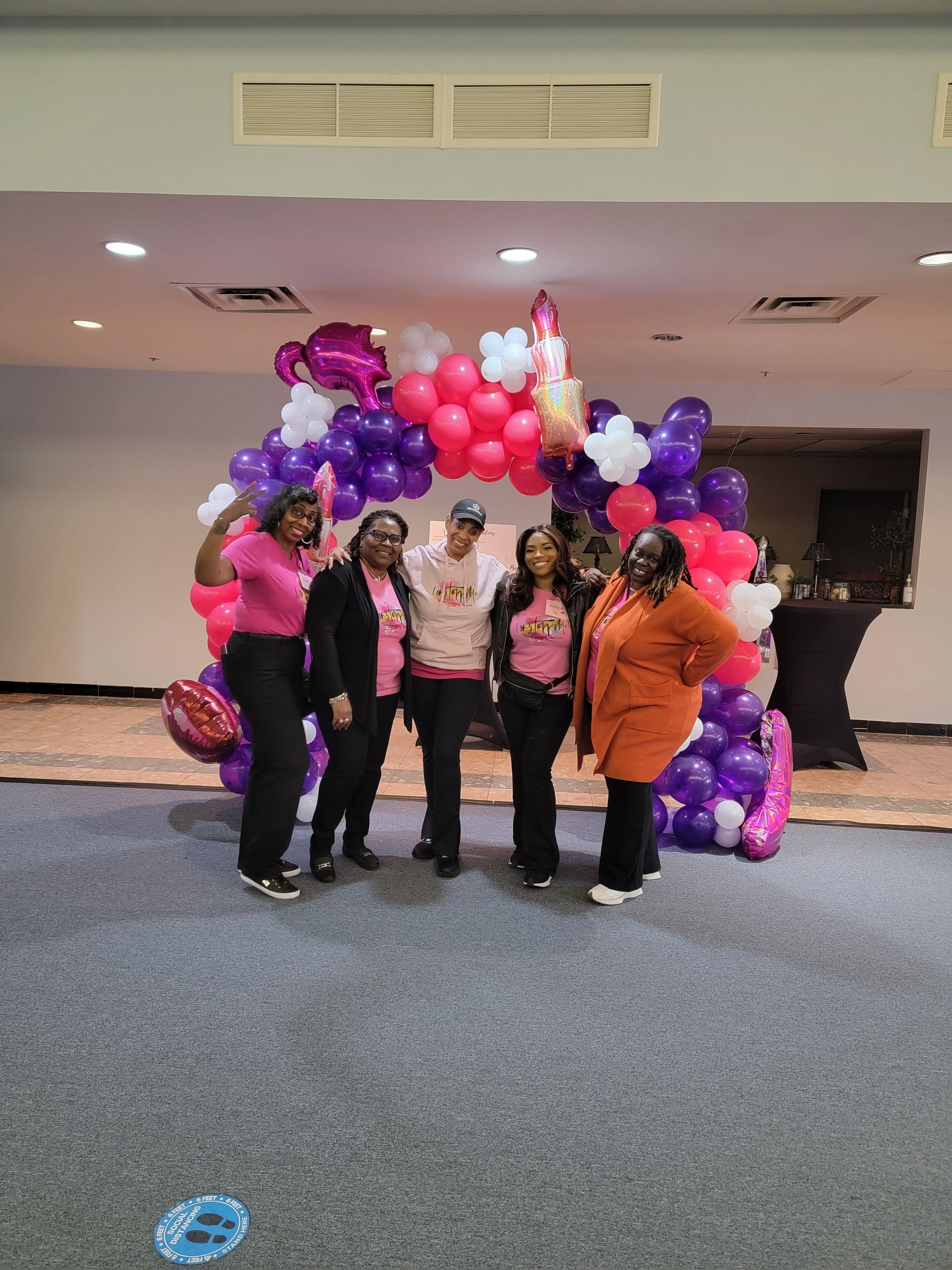 A group of women are posing for a picture in front of a balloon arch.