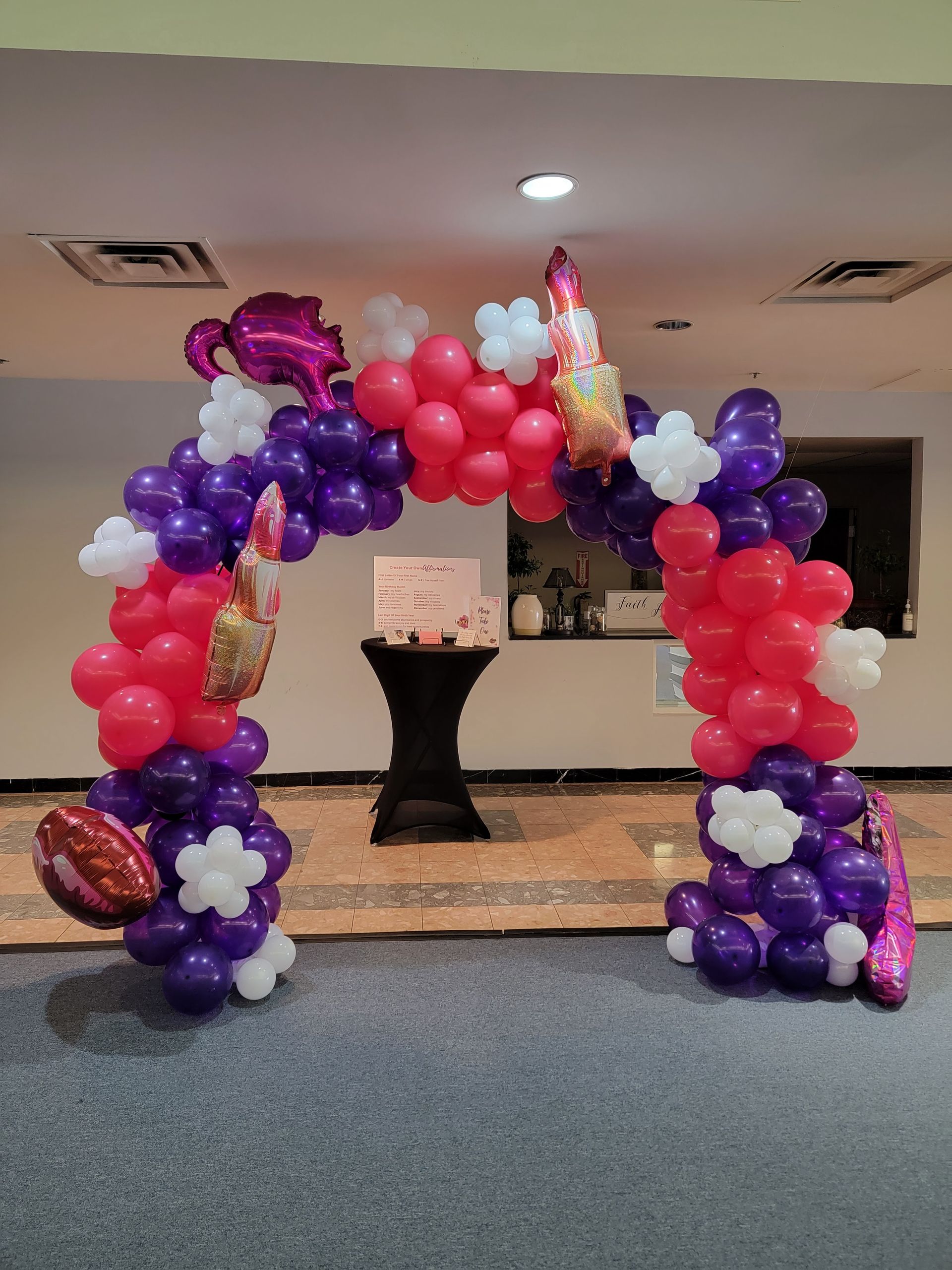 A red and purple balloon arch in a room with a table in the background.