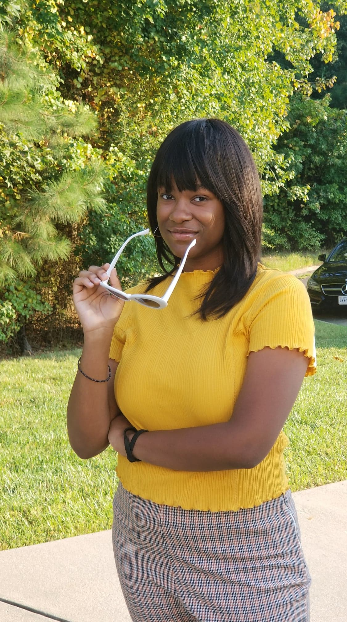 A woman in a yellow shirt is holding a pair of sunglasses.