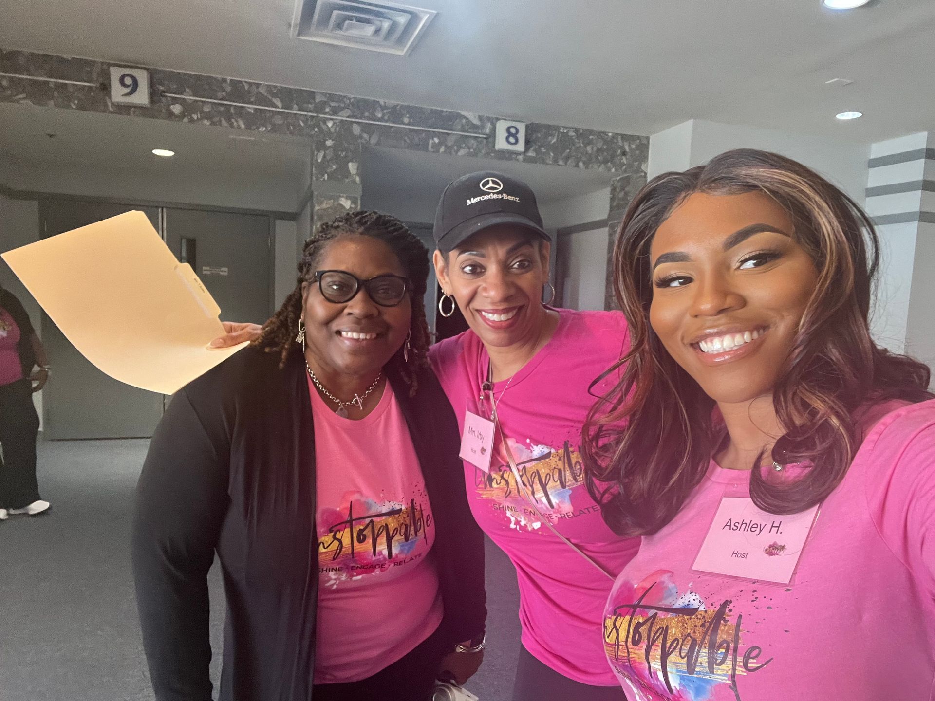 Three women wearing pink shirts are posing for a picture.