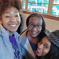 Three women are posing for a selfie in front of a stained glass window.