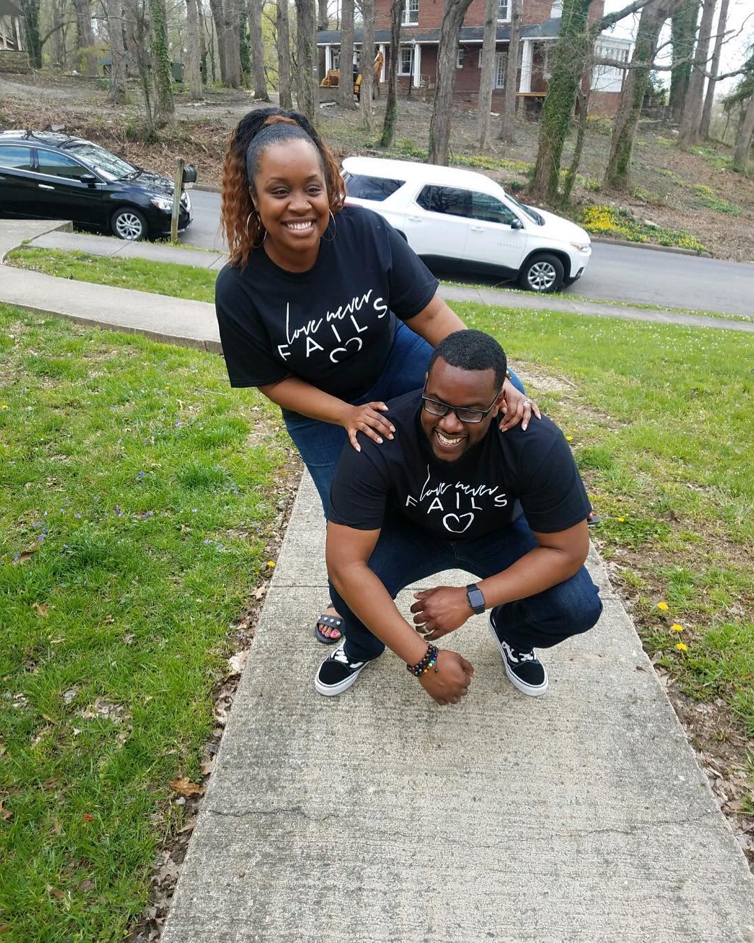 A man and a woman are posing for a picture on a sidewalk.