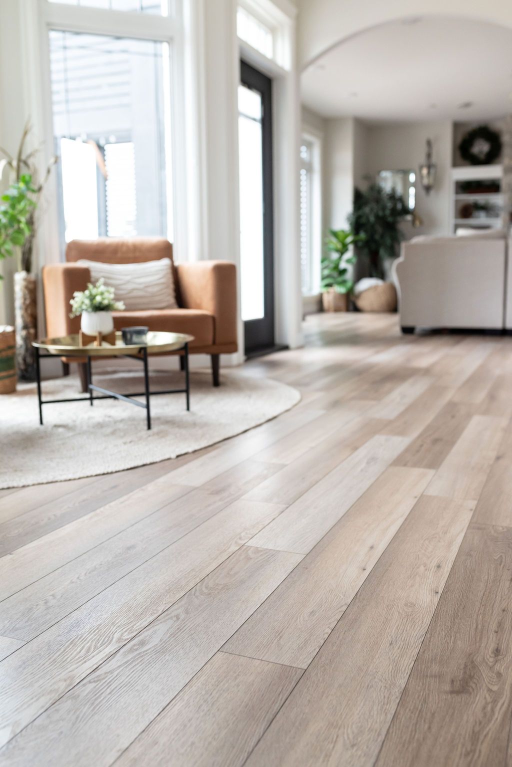Light wood-tone flooring in a living room with a leather armchair, round rug, and small coffee table.