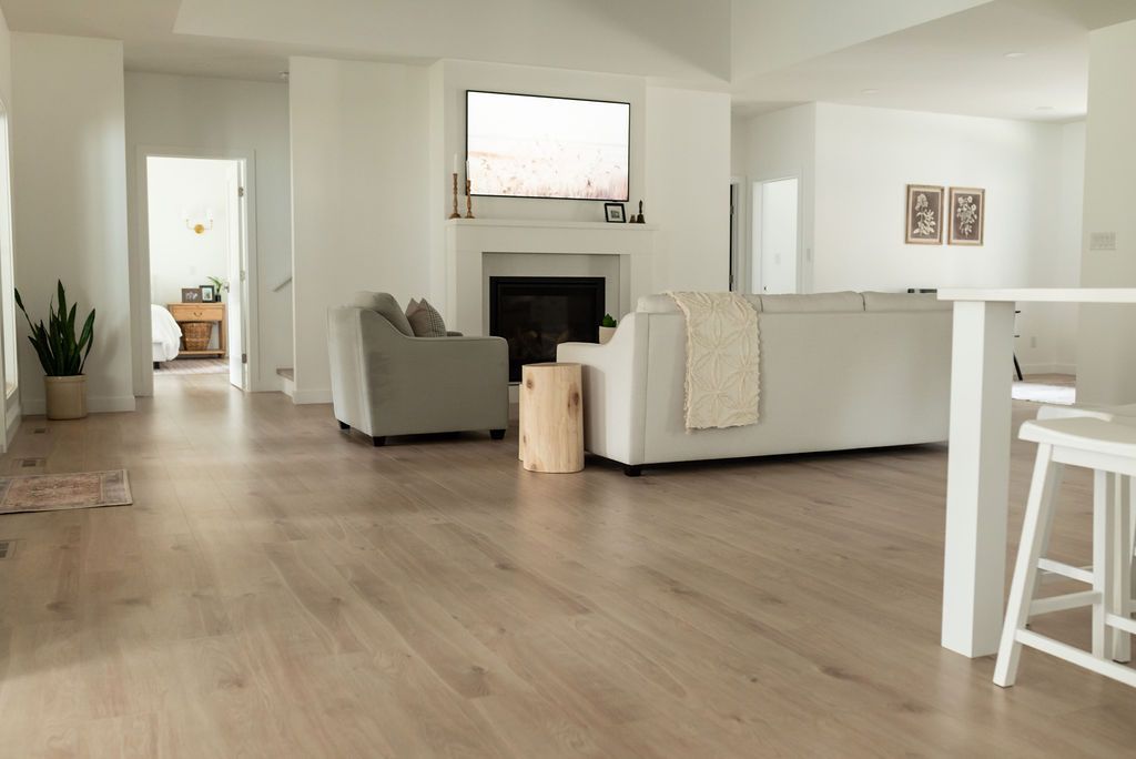 Spacious living room with light wood floors, white walls, fireplace, and neutral-toned furniture.