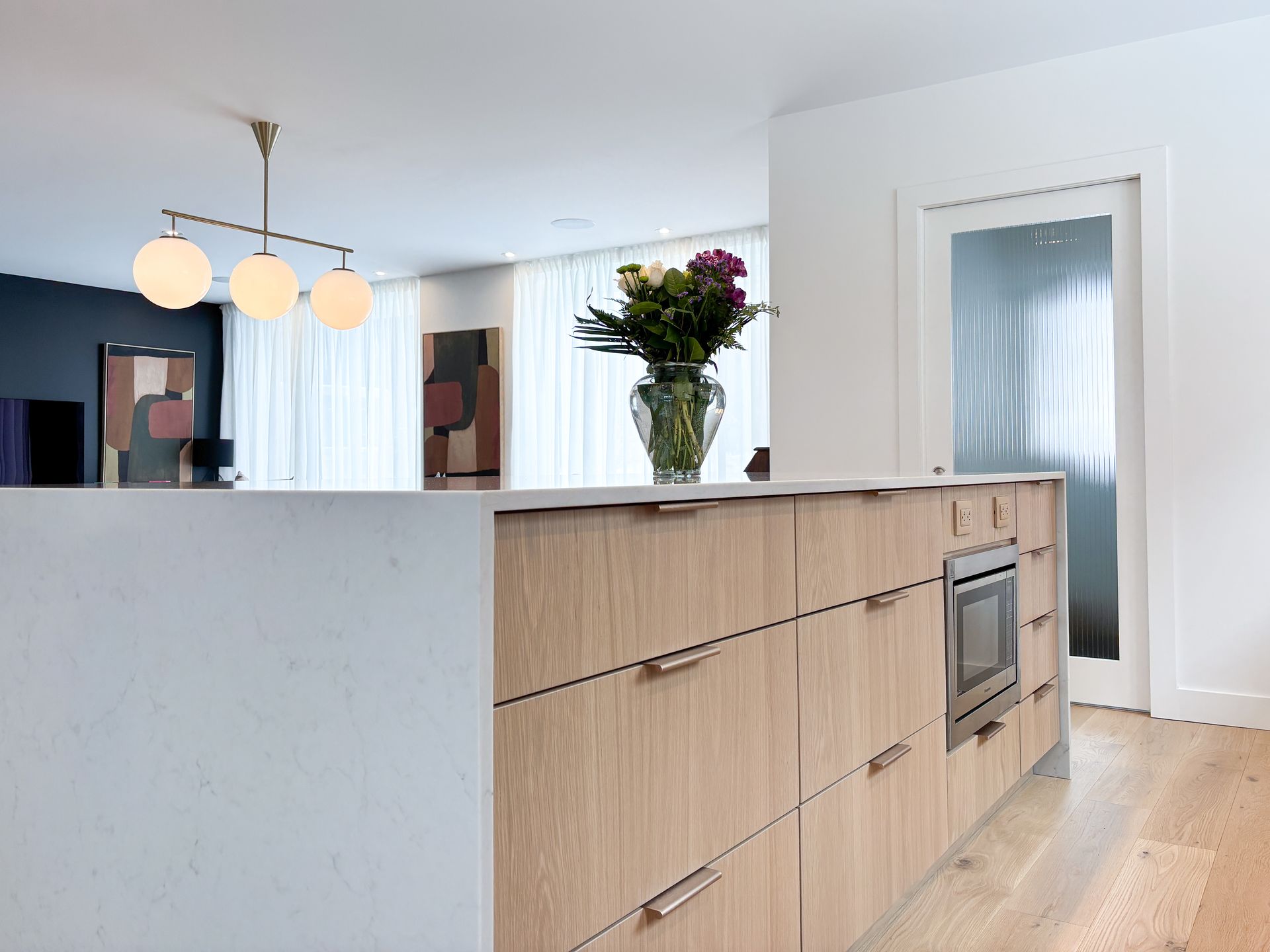 Îlot de cuisine moderne avec armoires en bois, micro-ondes intégré et vase de fleurs.
