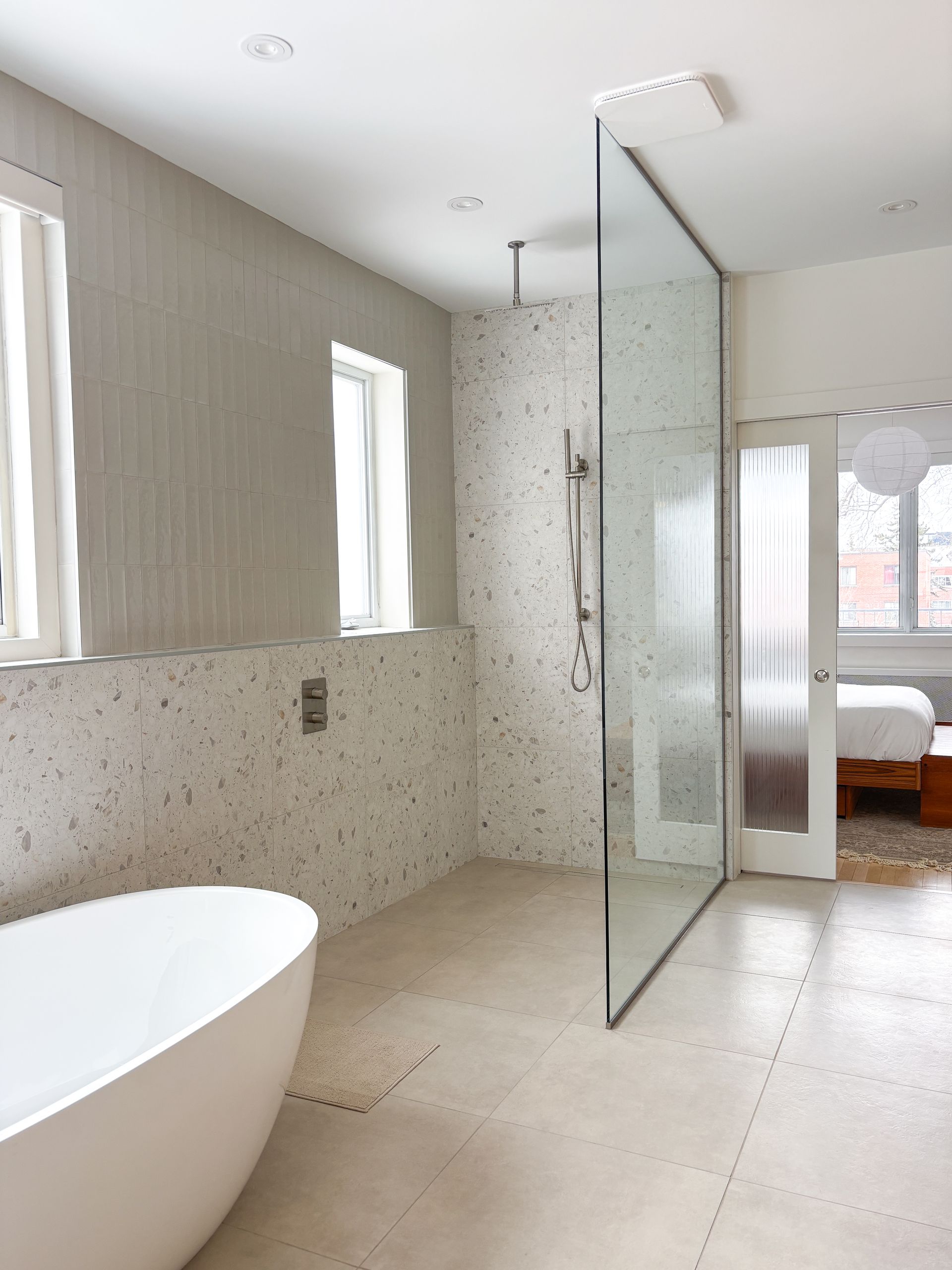 Salle de bain moderne avec baignoire autoportante et porte de douche en verre, couleurs neutres claires.