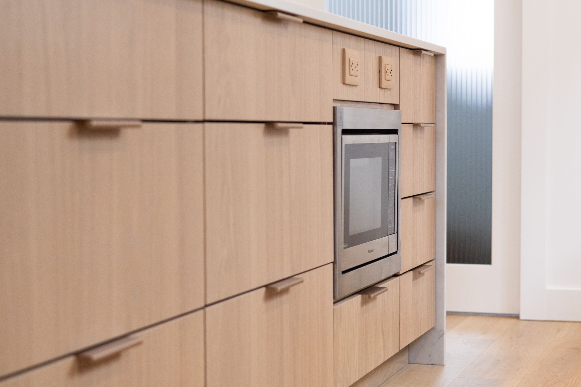 Armoires de cuisine en bois clair avec micro-ondes intégré et deux prises électriques.