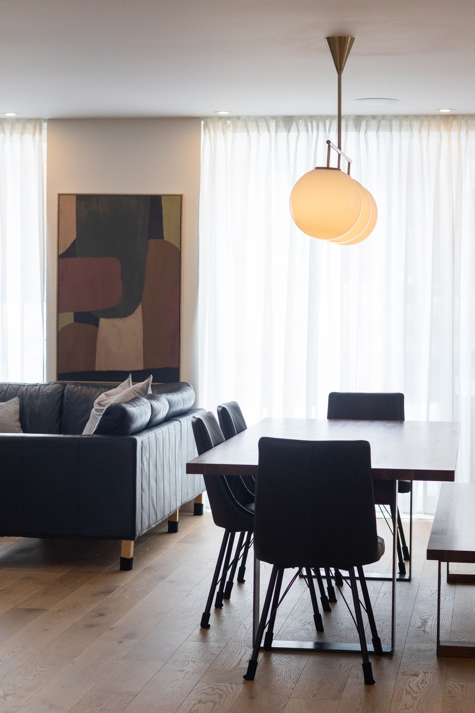 Salon et salle à manger avec meubles noirs, œuvres d'art et suspension ronde.