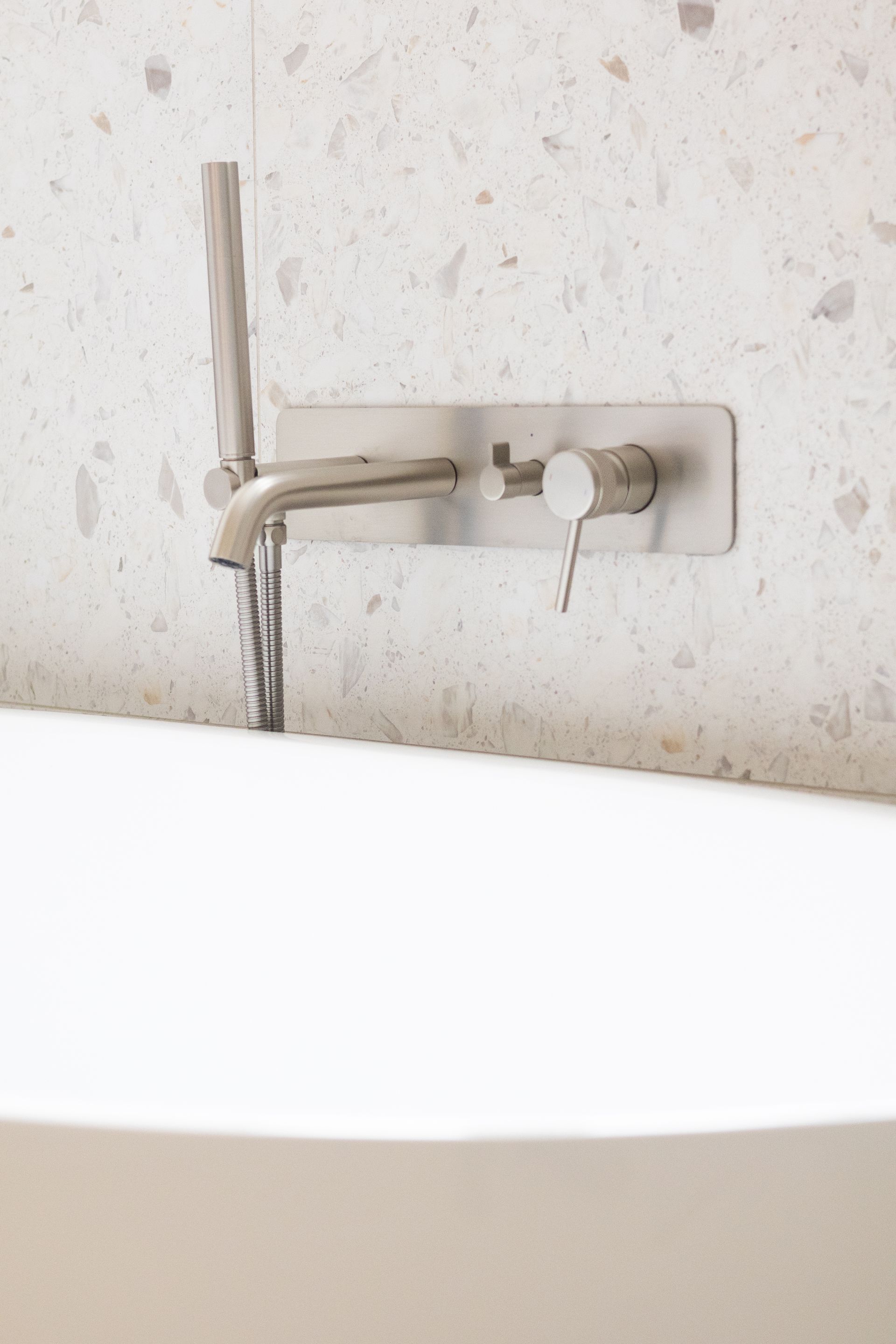 Robinet et pommeau de douche argentés montés sur un mur au-dessus d'une baignoire blanche.