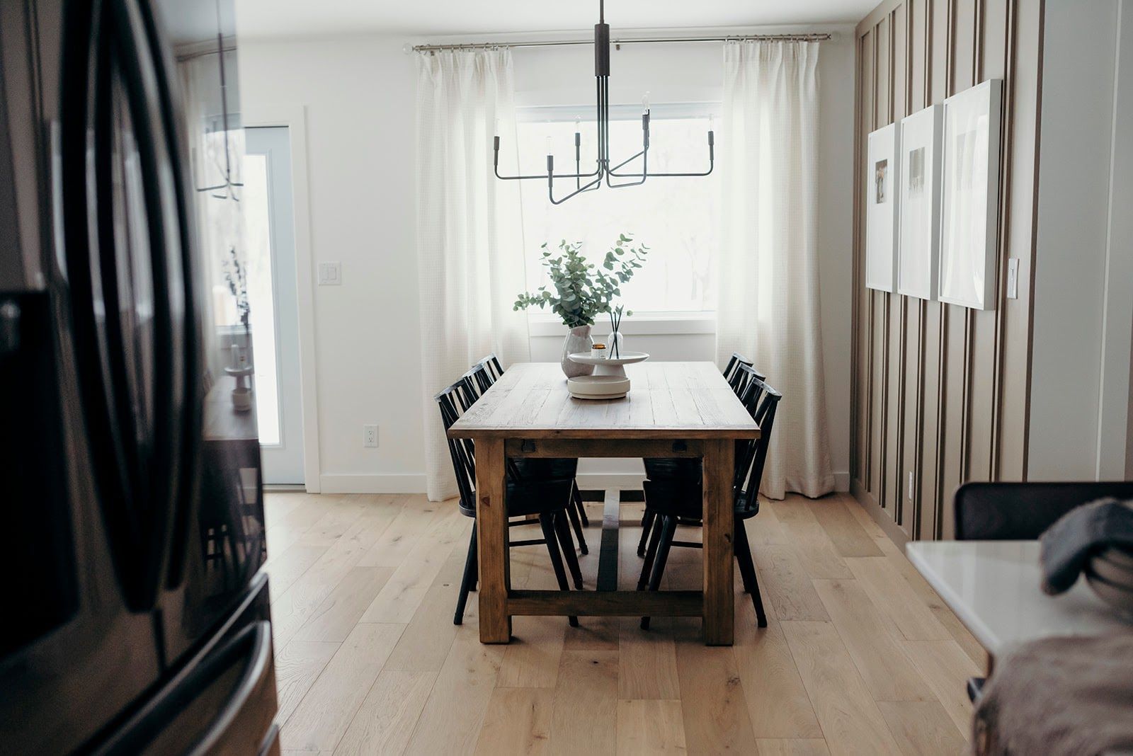 Dining room with wooden table and chairs, sheer curtains, and a chandelier.